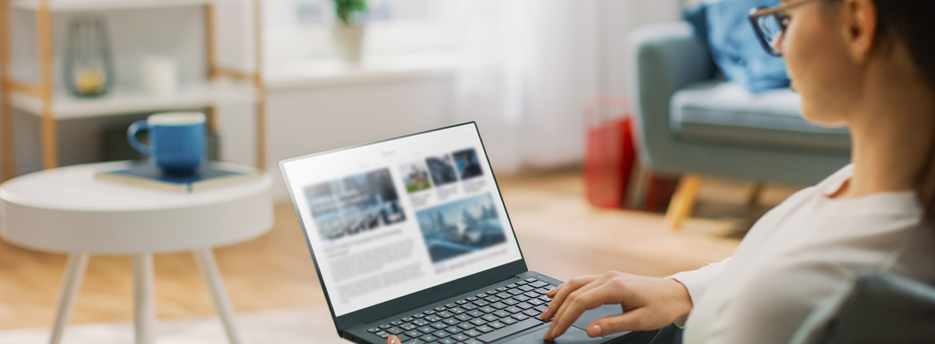 The image shows a laptop on a table with a person using it, set against an indoor background with furniture and decorative items.