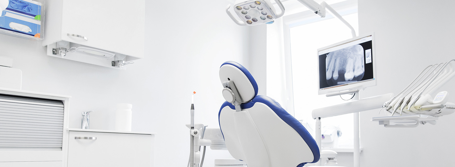 The image shows a modern dental office with advanced equipment, including a blue dental chair, a digital display screen, and a sleek, high-tech atmosphere.