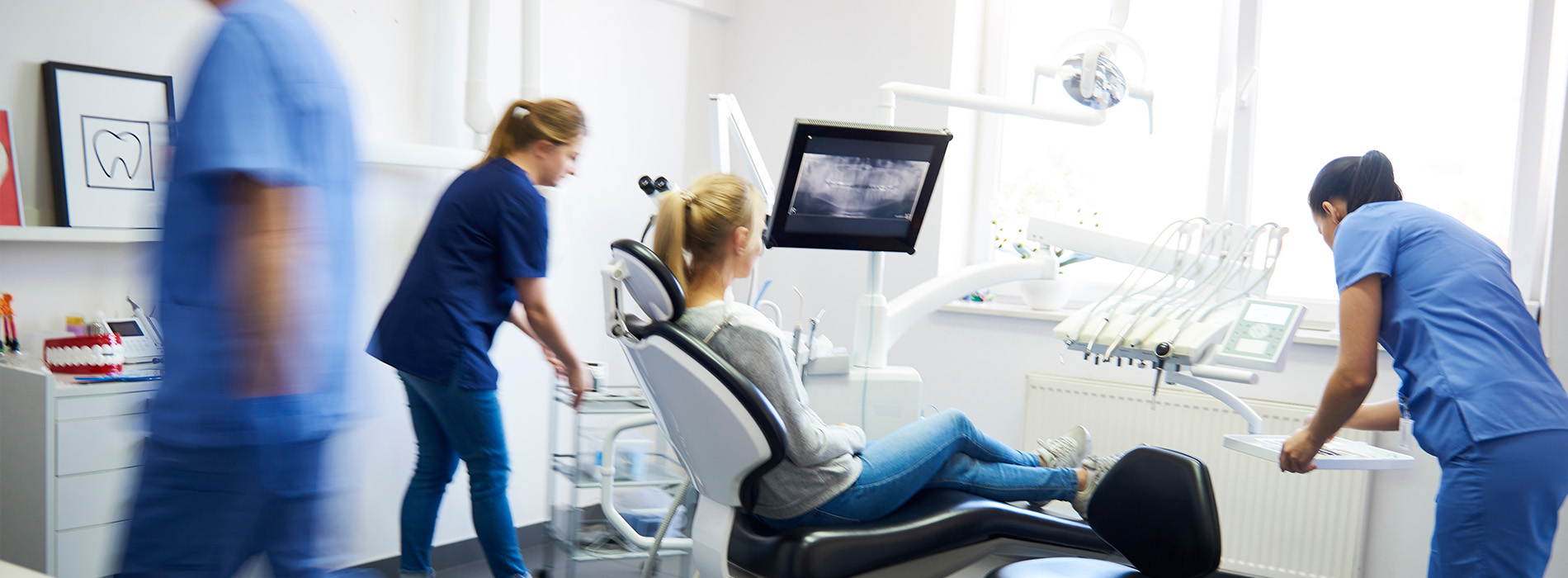 The image depicts a group of healthcare professionals in an office setting, with a focus on a dental chair and equipment, surrounded by various medical tools and devices.