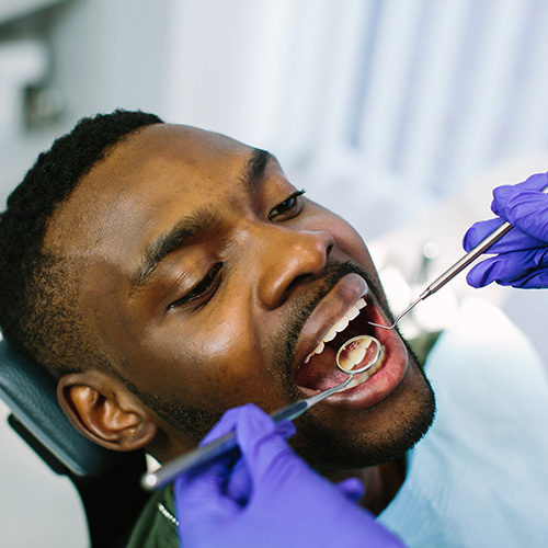 The image shows a person in a dental chair receiving dental care with a focus on their open mouth and the dental tools being used.