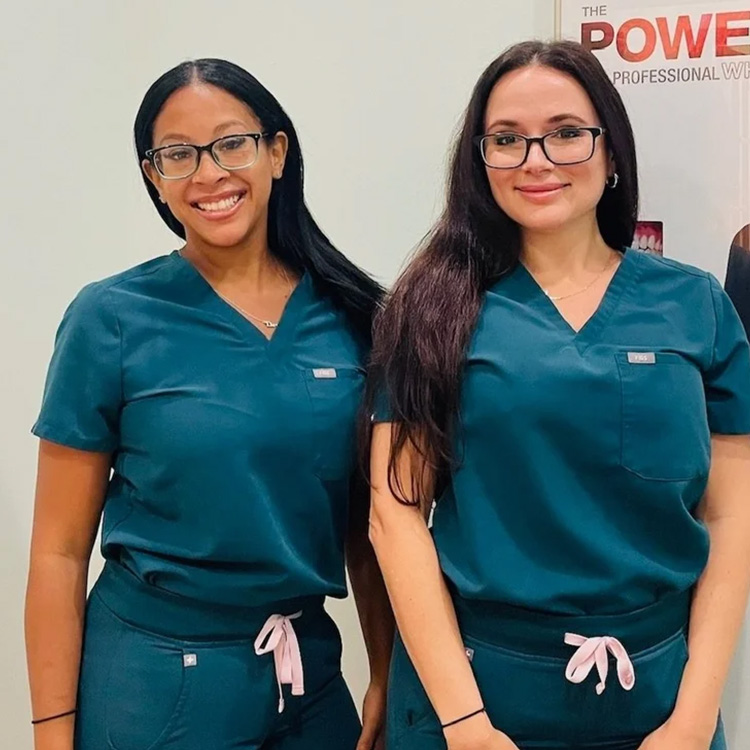 Two women wearing scrubs and smiling at the camera, posing together for a photograph.
