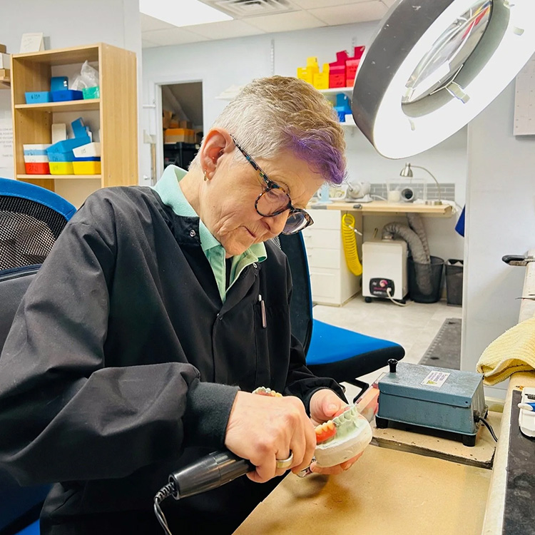 An elderly man working on a craft project at a workbench with tools and materials.