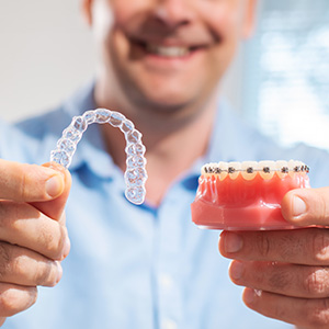 The image shows a person holding up a transparent dental retainer next to an inflatable gag, both with a toothy grin background.