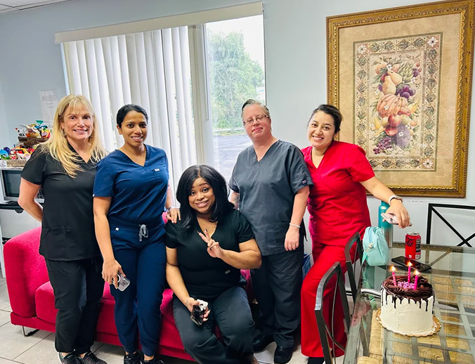 A group of people, presumably healthcare professionals, posing together in front of a cake with candles, celebrating an occasion in an office setting.