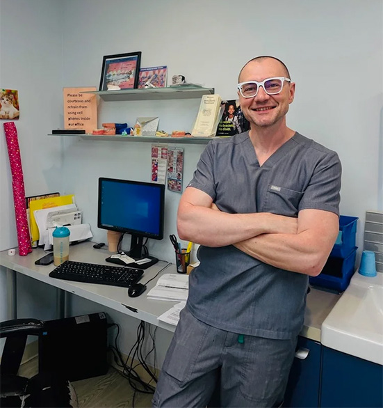 The image features a man standing in an office environment, wearing glasses, a stethoscope, and a white shirt, with his arms crossed over his chest.