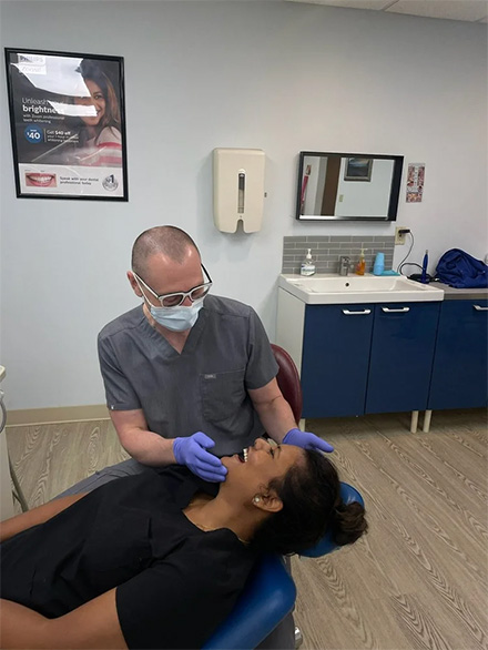 The image shows a dental professional wearing gloves, performing oral care on a patient lying on a dental chair.