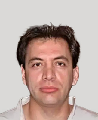 The image shows a man with dark hair and a beard, wearing a white shirt. He appears to be middle-aged, and his expression is neutral.