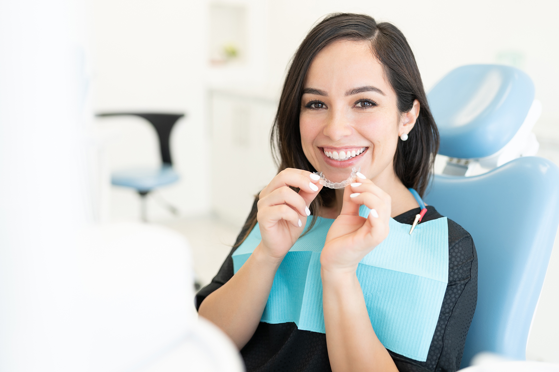 A dental hygienist at work, smiling and holding a toothbrush with blue bristles.
