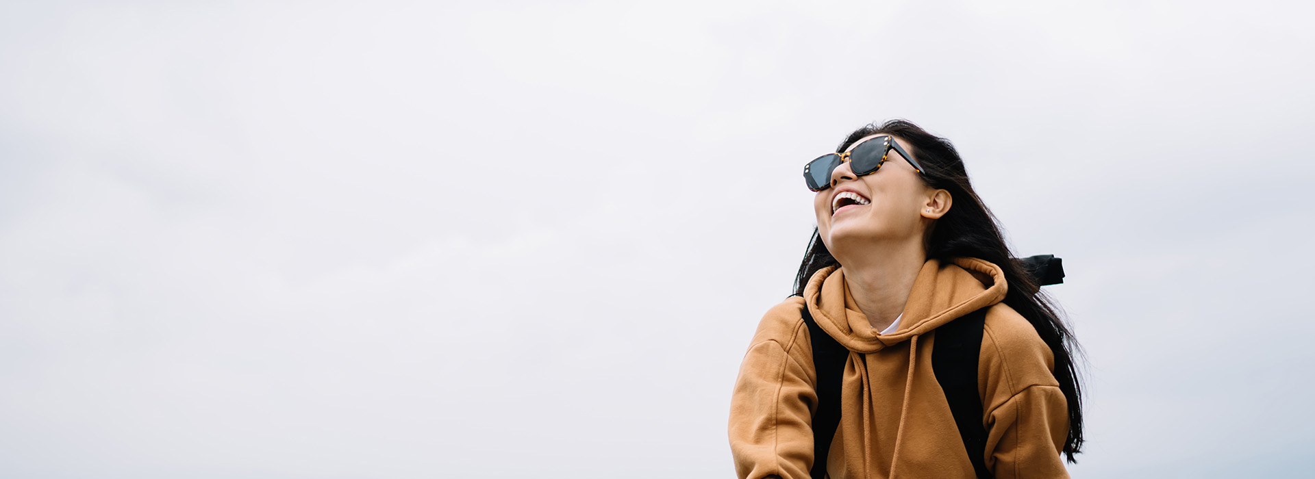A person wearing sunglasses and a backpack stands against a sky background.