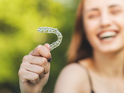 The image shows a person holding a toothbrush with a smiley face on it in front of a smiling face, possibly indicating dental hygiene or promotion.