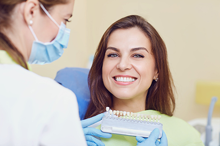 The image shows a woman sitting in a dental chair with a smile, receiving dental care from a professional who appears to be conducting a dental procedure.