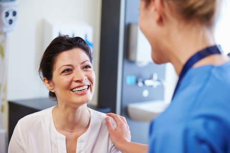 The image shows two individuals within a medical setting  a woman with a smile engages with another person who appears to be a healthcare professional, possibly during a consultation or examination.