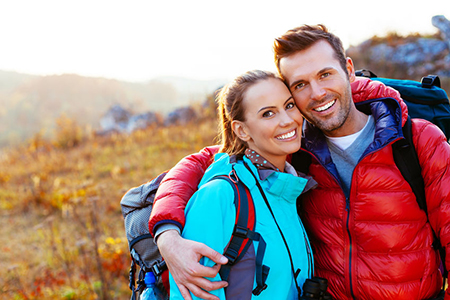 A man and woman are embracing outdoors during daylight hours, with both wearing backpacks and outdoor attire  they appear to be hikers.