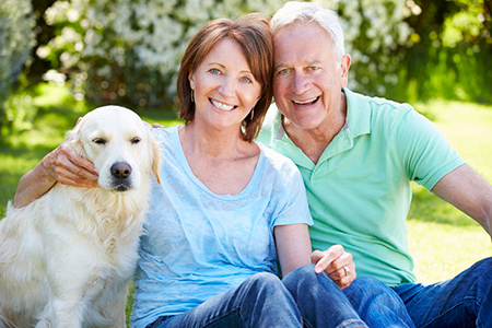 This image shows an elderly couple sitting outdoors with a golden retriever dog between them  they are smiling and appear to be enjoying each other s company.