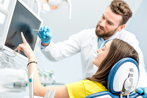 A woman in a dental chair, being attended to by a dentist who is pointing at something on her screen.