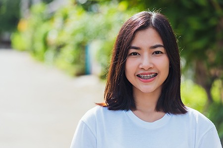 The image features a young woman with short hair smiling at the camera while standing outdoors during daylight.
