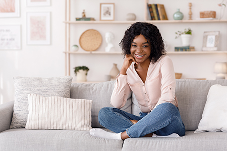 A young woman sitting on a couch with her legs crossed, smiling at the camera.