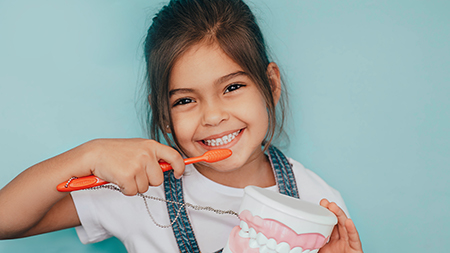 A young girl brushing her teeth with an oversized toothbrush and toothpaste.