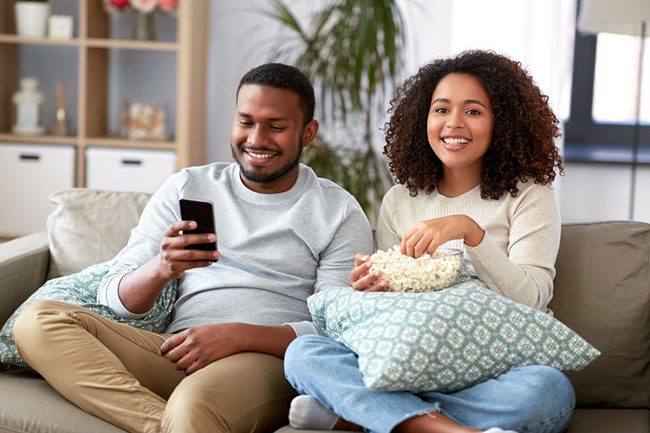 The image depicts a man and woman sitting on a couch, engrossed in watching something on a smartphone.
