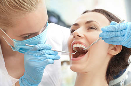 A woman receiving dental treatment from a dental professional, with both individuals wearing face masks.