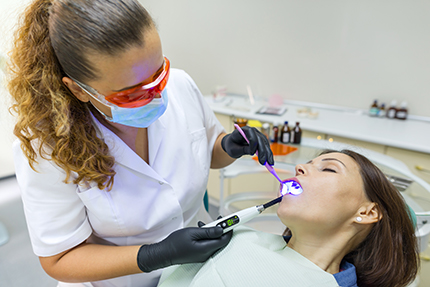 Dentist performing dental procedure on patient s teeth, with both individuals wearing face masks and using dental tools.